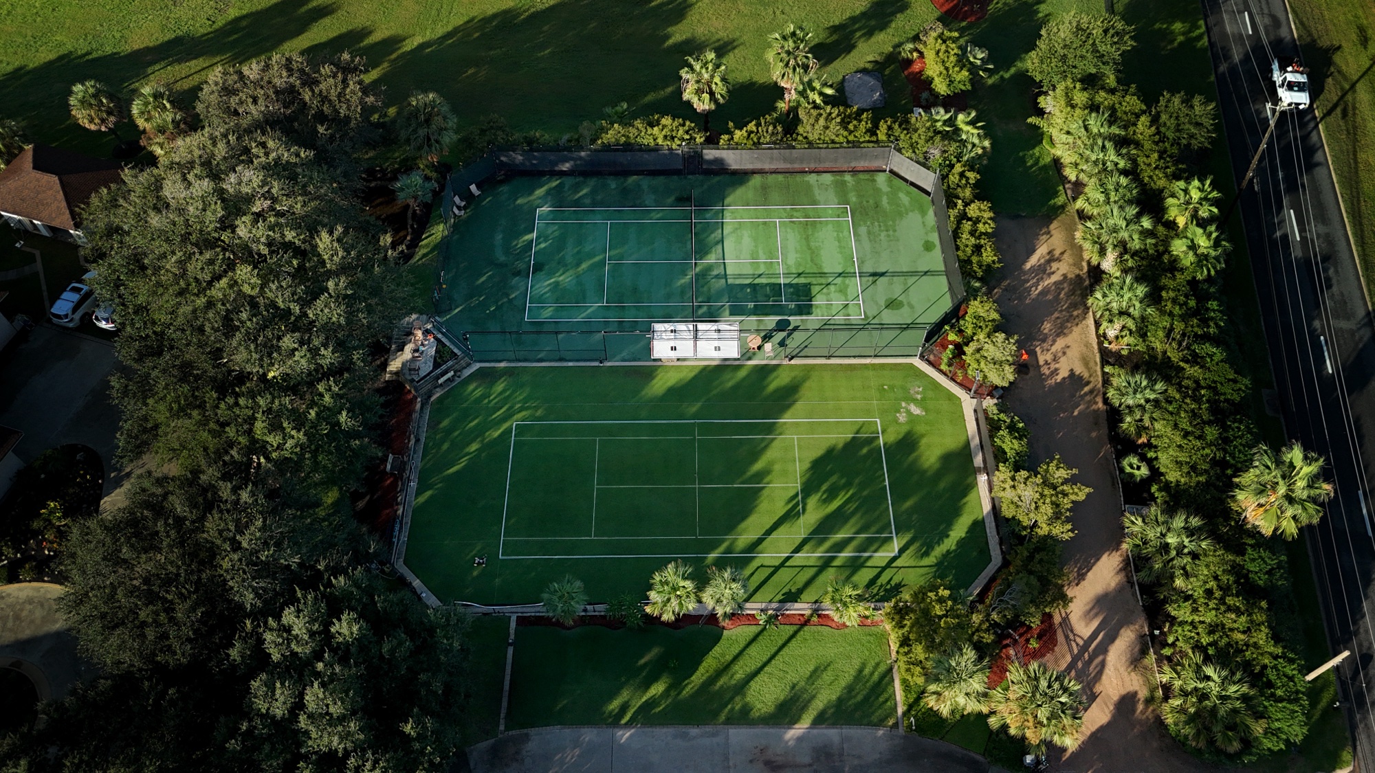 Both courts from the air, screened from the road by trees