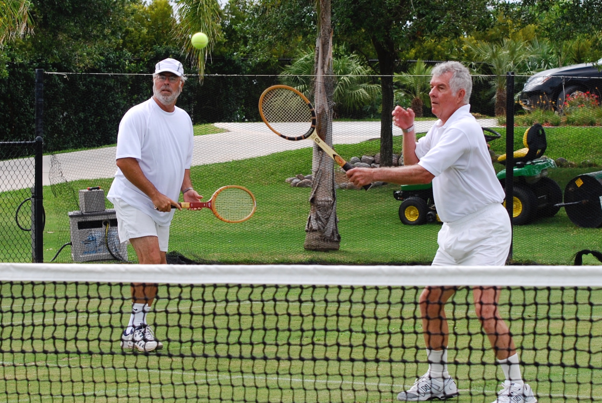 Two players in whites with wooden racquets at the net